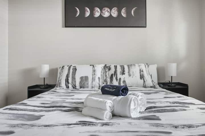 Minimalistički uređena spavaća soba s bračnim krevetom na kojem je moderna jednobojna posteljina, blagom rasvjetom i umjetničkim djelom na zidu koje prikazuje mjesečeve mijene. Čisti ručnici i ručnik za uklanjanje šminke gostima pružaju udobnost i osjećaj mirnog i elegantnog boravka.