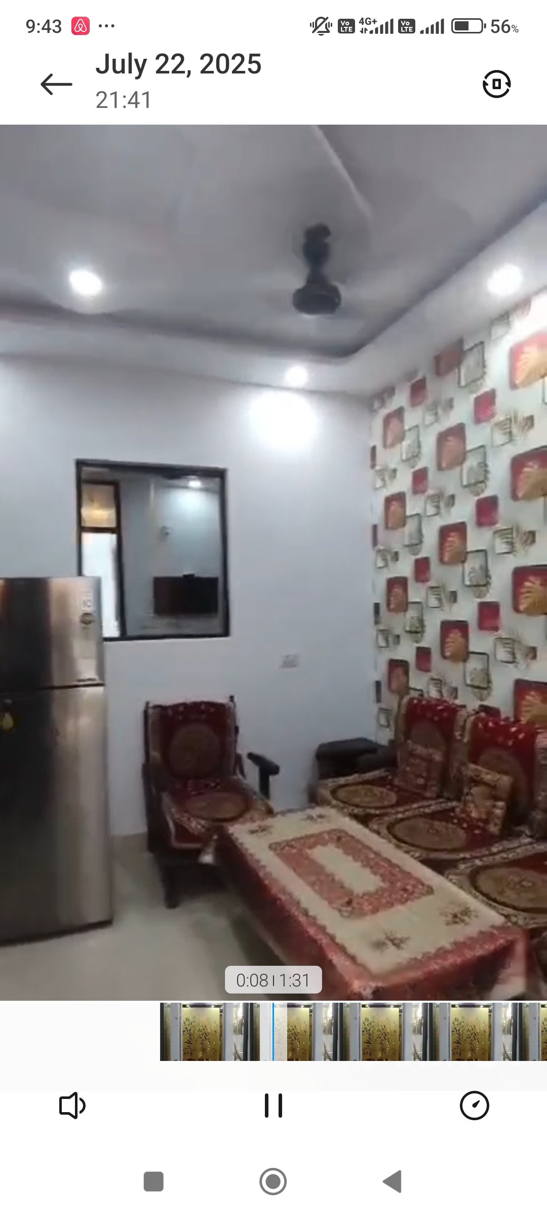 A welcoming living area features decorative wallpaper with a floral pattern. Comfortable seating arrangements include several upholstered chairs and a small table. A modern refrigerator is situated next to a window, allowing natural light to illuminate the space.