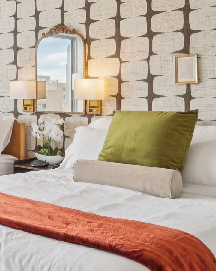 МЕКА СВЕТЛИНА, УЮТНИ АКЦЕНТИ. Подредените една върху друга възглавници, кадифената възглавница и двойните бракнери, които заобикалят двойните легла, създават уютна обстановка, която изглежда като в бутик хотел, а не като обикновена спалня.
