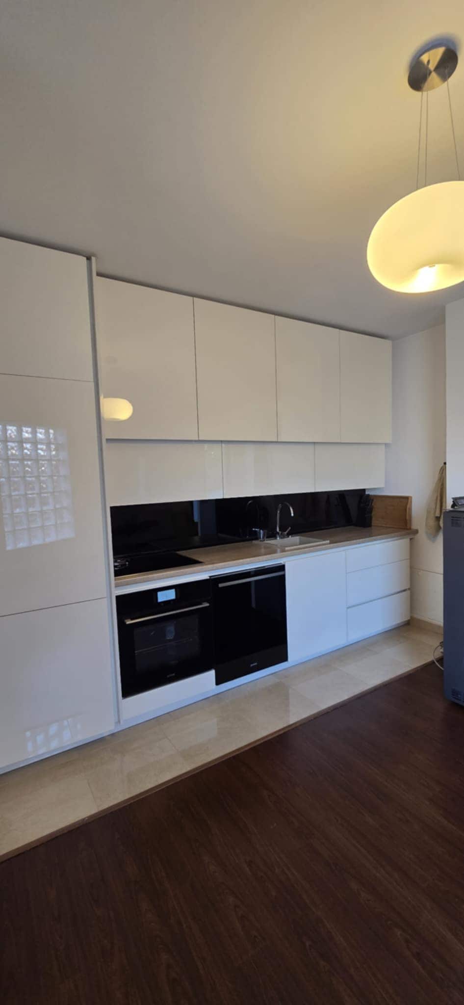 A modern kitchen is equipped with sleek white cabinetry and a combination of black and stainless steel appliances. A built-in oven and stovetop are located beneath the countertop, while a refrigerator sits adjacent to the cabinetry. Soft lighting enhances the clean lines and functionality of the space.