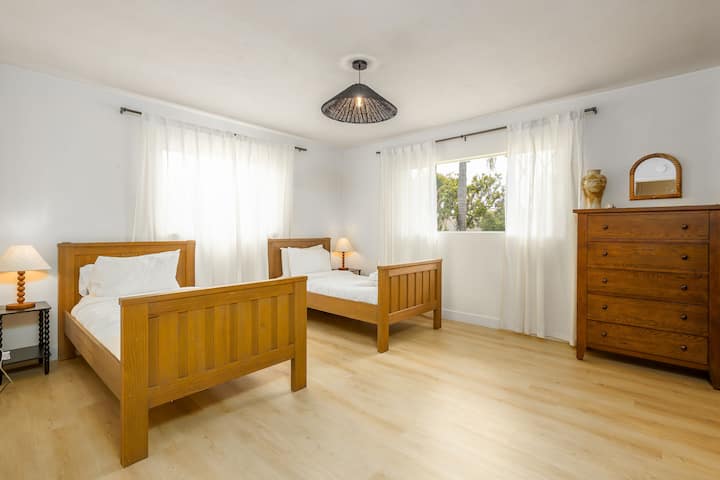 توفر غرفة النوم المشرقة ذات التهوية الجيدة ملاذًا مريحًا مع سريرين خشبيين مريحين، مما يجعلها مثالية للأصدقاء أو العائلة. 