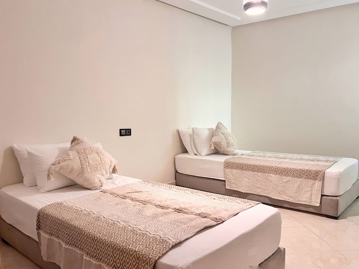 Svijetla spavaća soba s 2 jednostruka kreveta (mogu se spojiti u bračni krevet). Dekoracija u bež i bijelim tonovima, profinjena posteljina i marokanski detalji za maksimalnu udobnost.