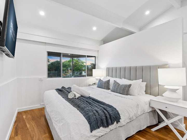 غرفة نوم رئيسية مع سرير كينج وتلفزيون وخزائن ملابس له ولها وإطلالات هادئة على الحديقة.