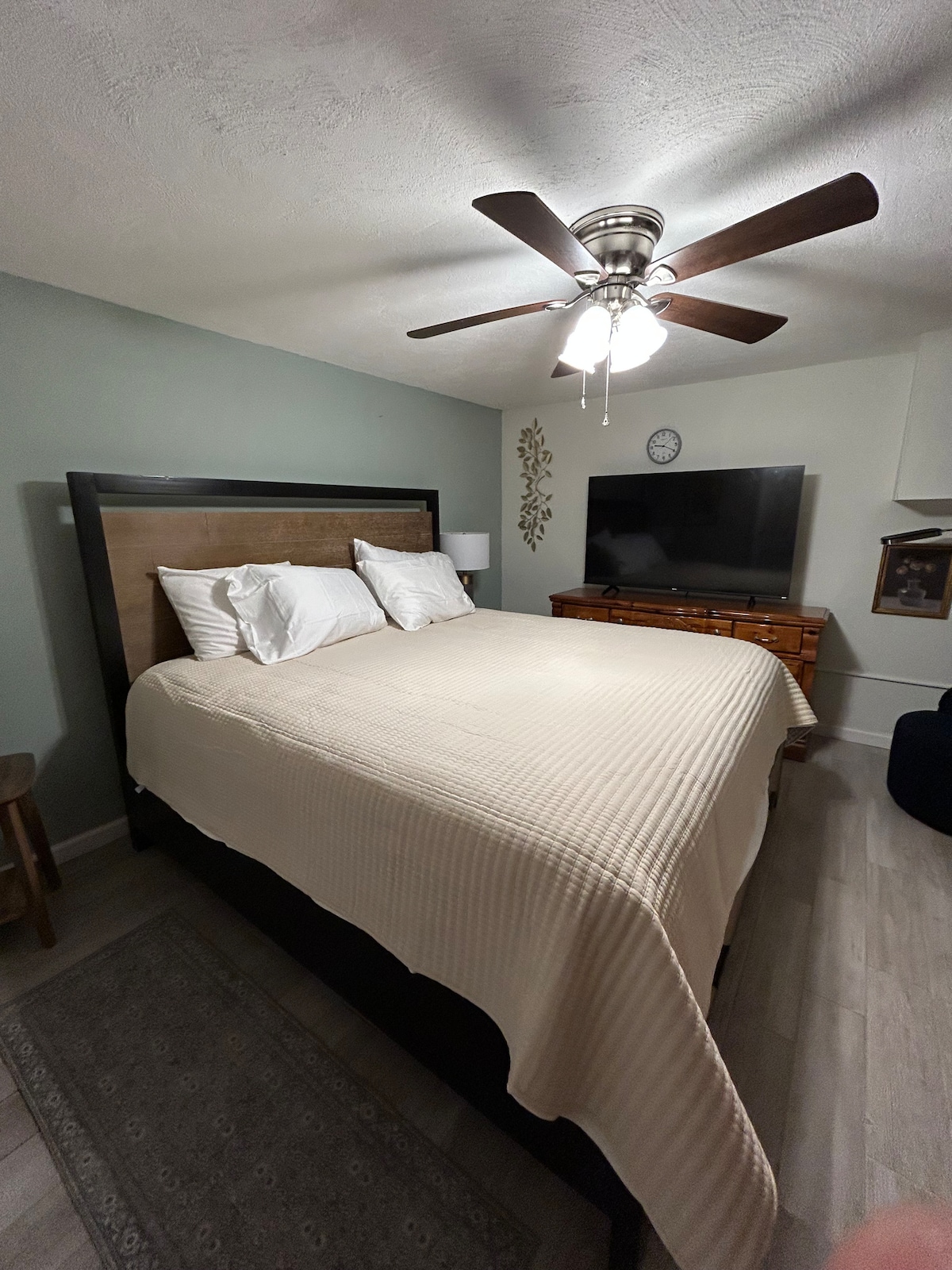 King bedroom — cream comforter, 55-inch TV, sage green walls, ceiling fan