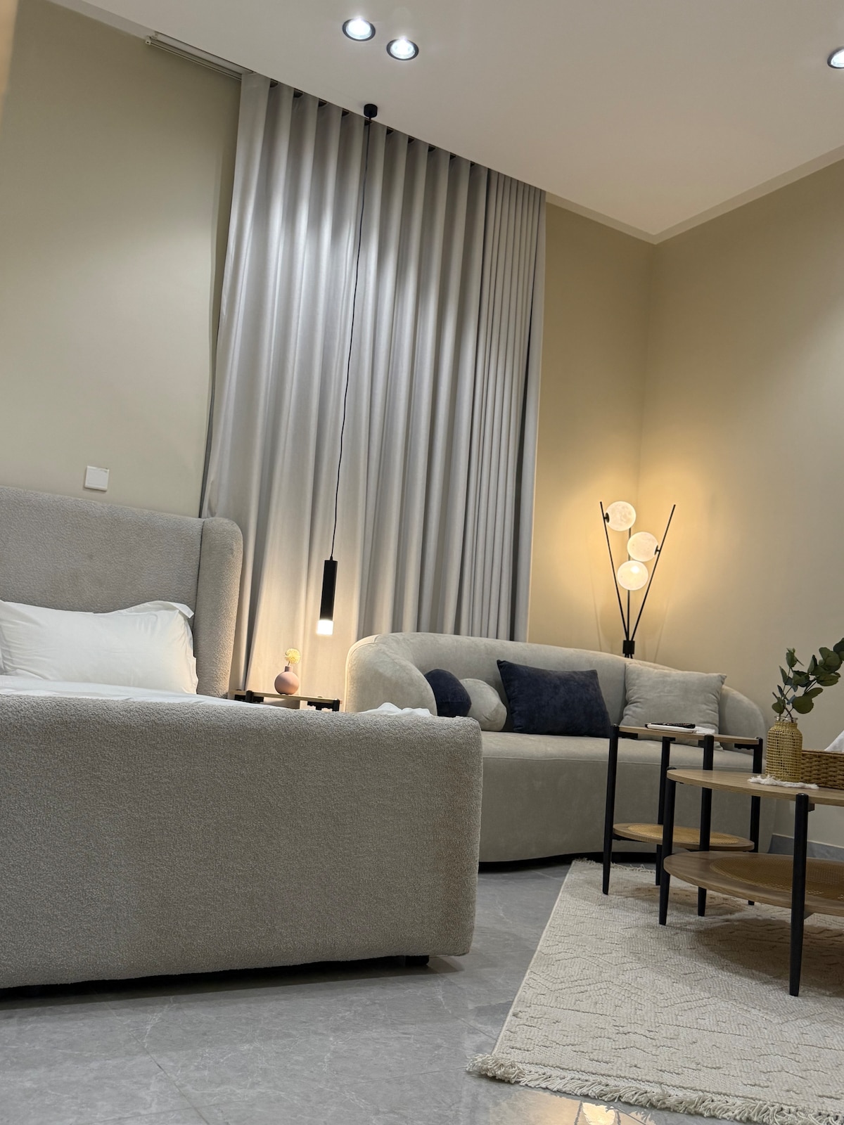 A modern seating area is featured, with a plush sofa and a cozy armchair. A soft rug is positioned on sleek gray tiles. The space is illuminated by a standing floor lamp next to a coffee table, enhancing the room's comfortable ambiance.