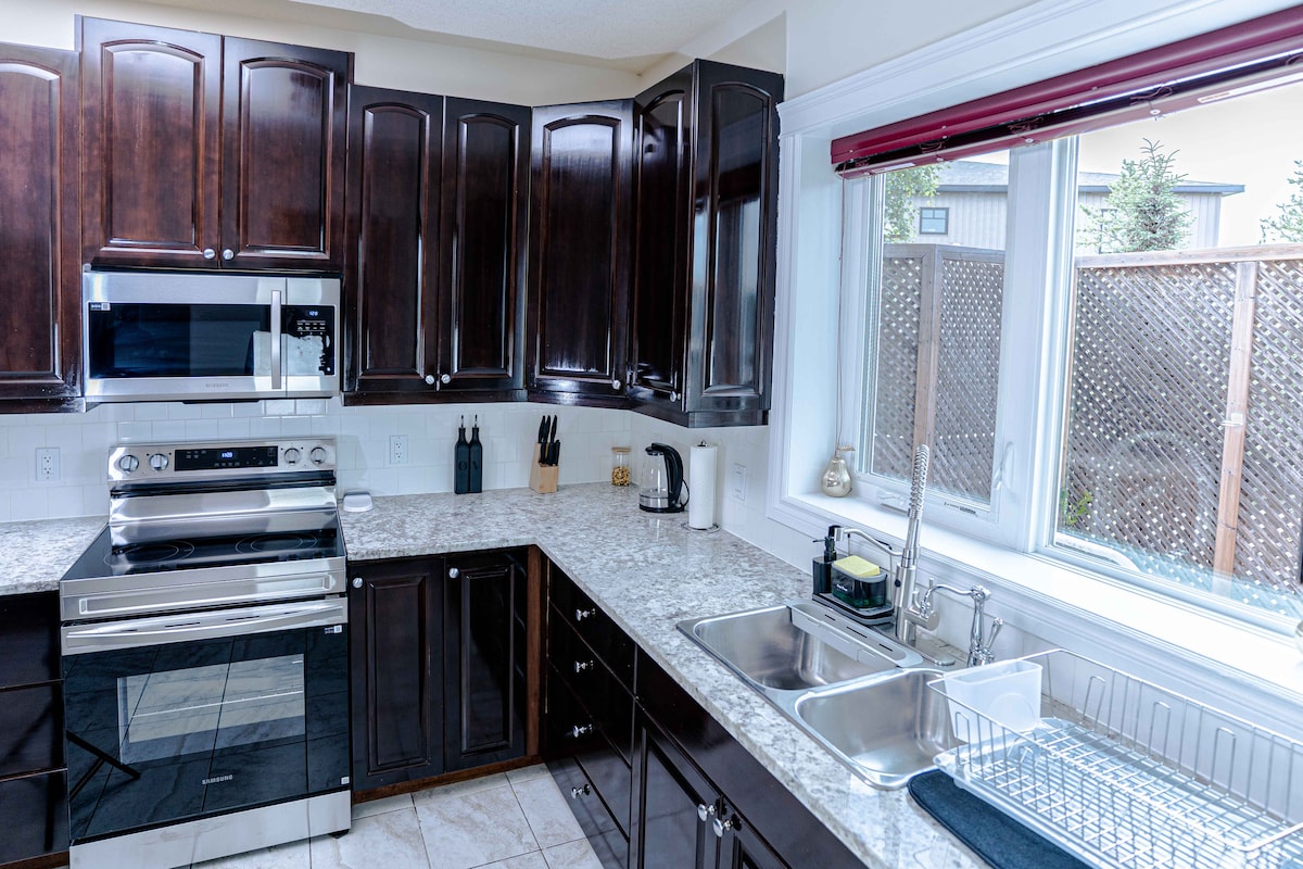 The kitchen features dark wood cabinetry complemented by granite countertops. Modern appliances, including a microwave and oven, are visible. A double sink sits beneath a window, providing natural light. Counter space is neatly organized with essential utensils and a dish drying rack.