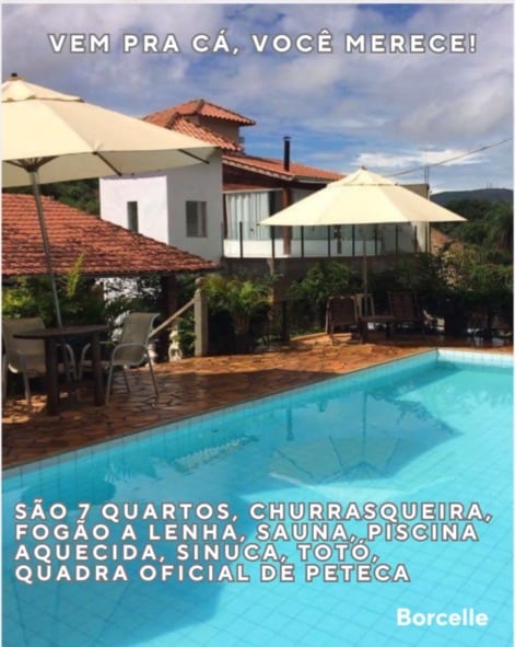 A clear swimming pool, measuring 10x5 meters, reflects the surrounding greenery and is framed by two lounge chairs. The rustic exterior of a multi-level building with a terracotta roof is visible in the background, along with a patio area ideal for relaxation.