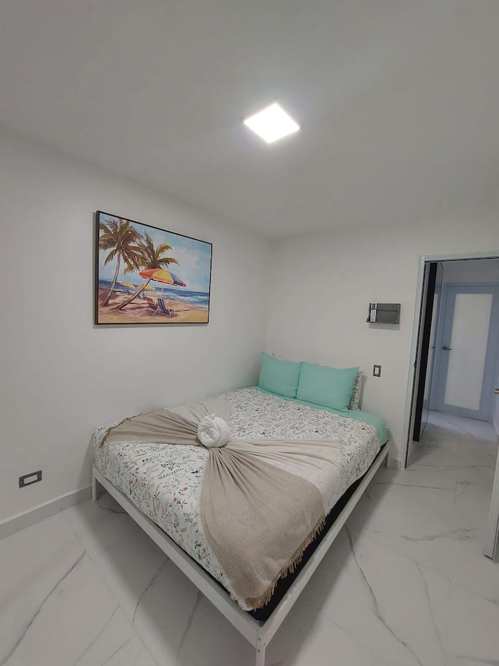 غرفة نوم كوين بأجواء استوائية
سرير بحجم كوين مع فن جداري بطابع الشاطئ وألوان محايدة ناعمة، مما يخلق شعورًا ساحليًا هادئًا.