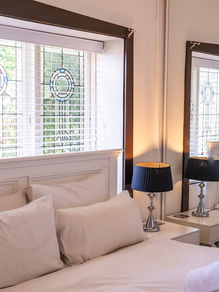 Coin chambre confortable avec une literie moelleuse, des vitraux élégants et une lampe de chevet stylée qui se reflète dans le miroir. ️✨ Un espace lumineux et serein, parfait pour le repos et la détente.