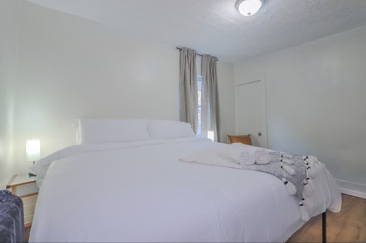 Dormitorio tranquilo y minimalista en Lakewood Airbnb con una cómoda cama tamaño king, sábanas blancas suaves y cortinas opacas para una noche de sueño reparador. Perfecto para los huéspedes que aprecian un espacio tranquilo y ordenado.