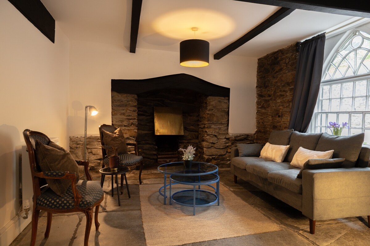 Dhomë ndenjjeje komode dhe rustike me mure guri të ekspozuar dhe një oxhak të ngrohtë në qendër.