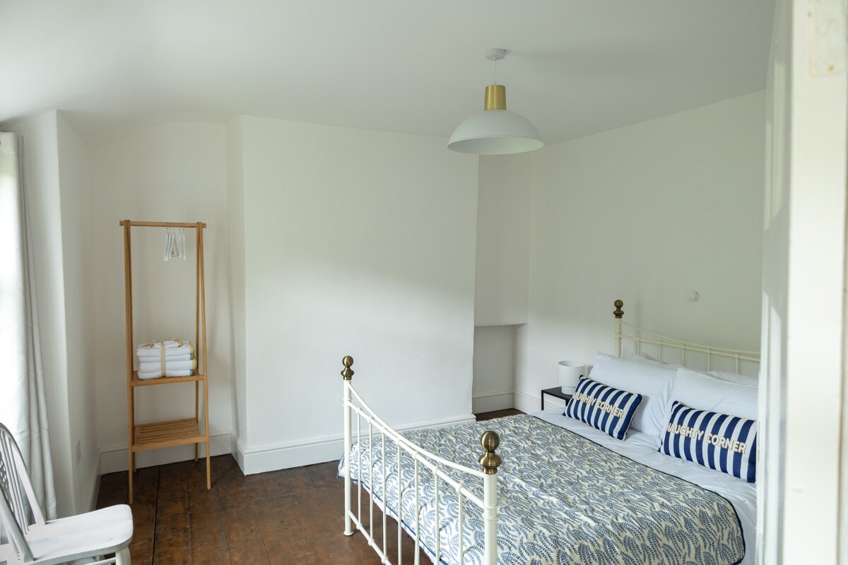 Dhomë gjumi e ndritshme me një krevat të bardhë metalik dhe dekor të freskët dhe të ajrosur.