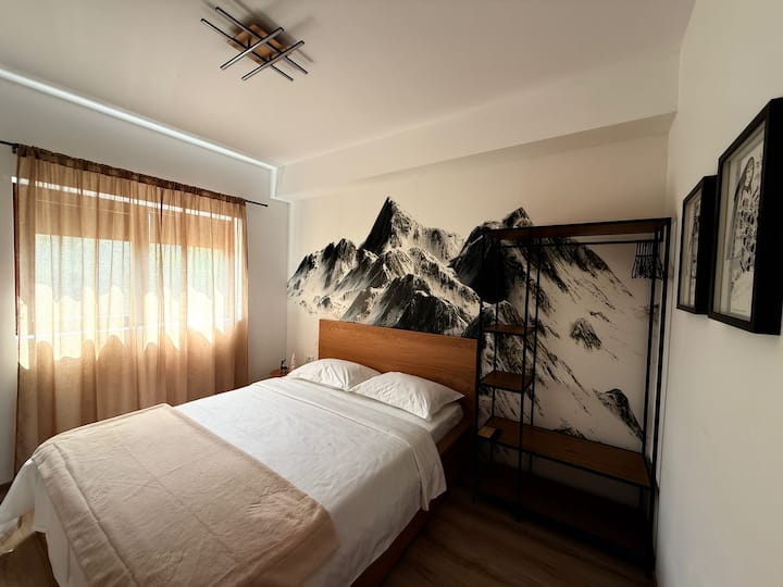 Questa camera da letto offre ispirazione e comfort, con un suggestivo murale di montagna dietro il letto e una grande Smart TV per le serate di cinema sotto il piumone.

