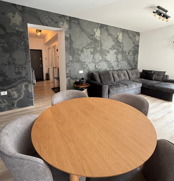 Una zona giorno luminosa e open space con comodi posti a sedere, un generoso tavolo da pranzo per quattro persone e un'elegante parete d'accento. L'enorme Smart TV Full HD completa la configurazione di intrattenimento per i tuoi cari