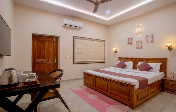 Bedroom 1 – Gulabi Mahal: Spacious and elegant, featuring a large wooden bed, maroon and white bedding, framed artwork, and ambient lighting that creates a warm, inviting atmosphere with a touch of royal charm.