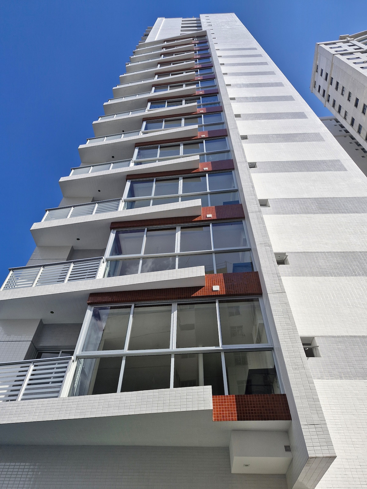 The building features a modern design with multiple floors and large glass windows. The clean lines of the facade are complemented by red accents, reflecting a contemporary architectural style under a clear blue sky.