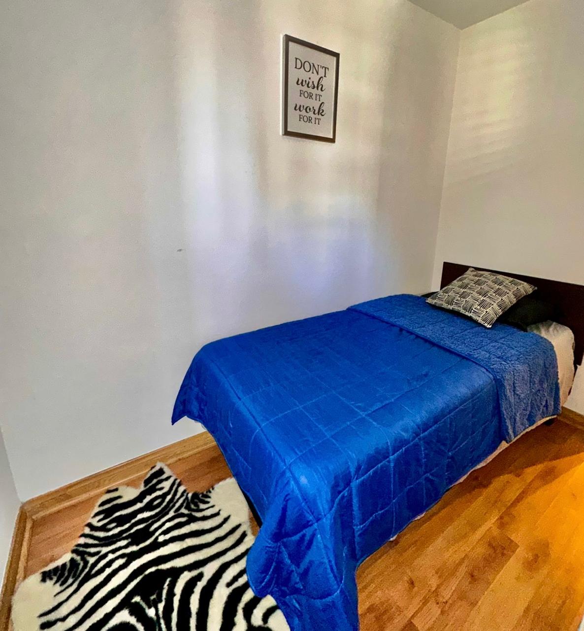 Dhomë gjumi kompakte dhe e ndriçuar me një krevat tek, një komodinë, një dollap të madh dhe një banjë brenda suitës. Dekor minimalist me një fotografi në mur dhe një abazhur modern; hapësirë e rregullt dhe funksionale për një person