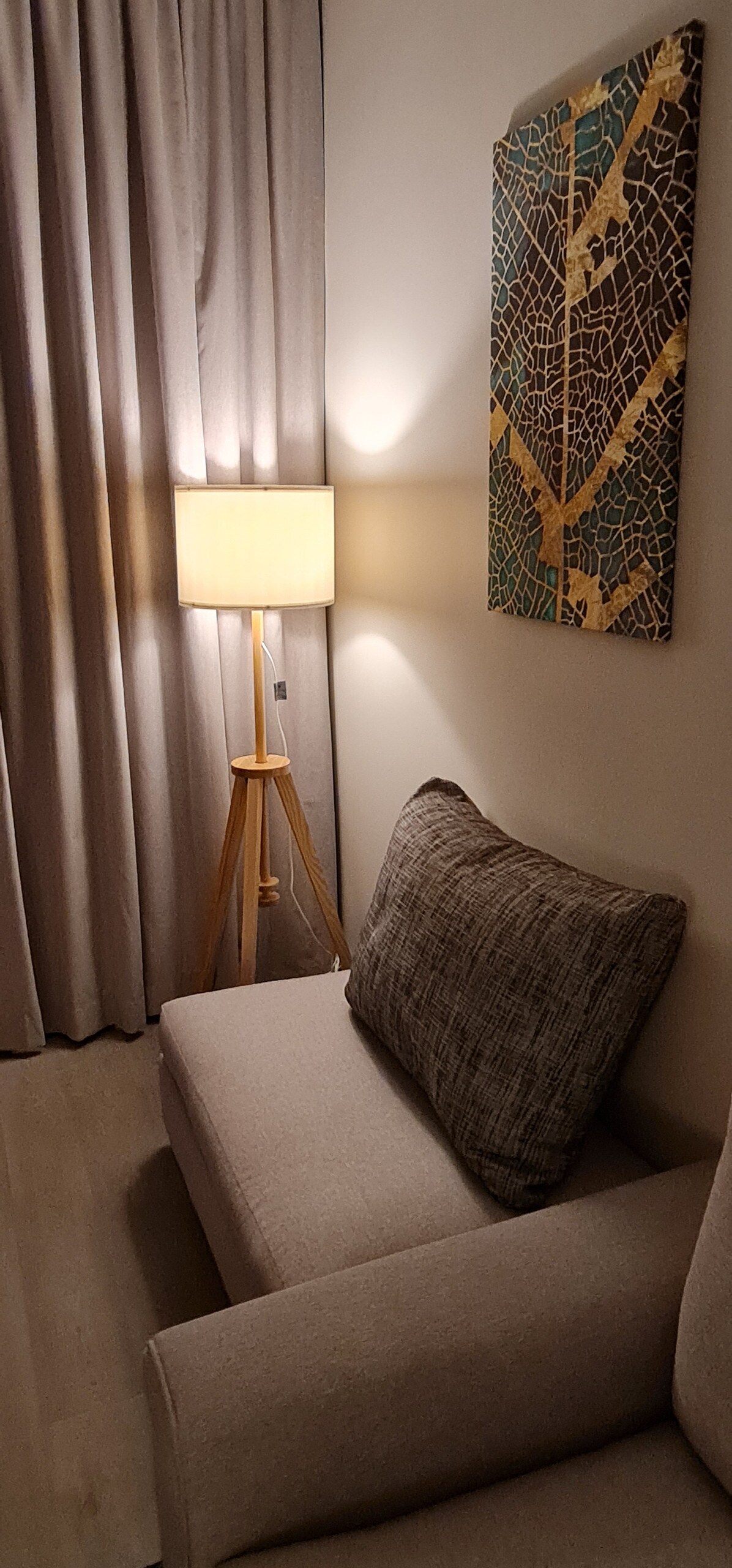 A cozy seating area is highlighted by a light-colored sofa adorned with a textured cushion. A standing lamp provides soft illumination beside the sofa, and elegant curtains frame the window, allowing for a peaceful atmosphere.