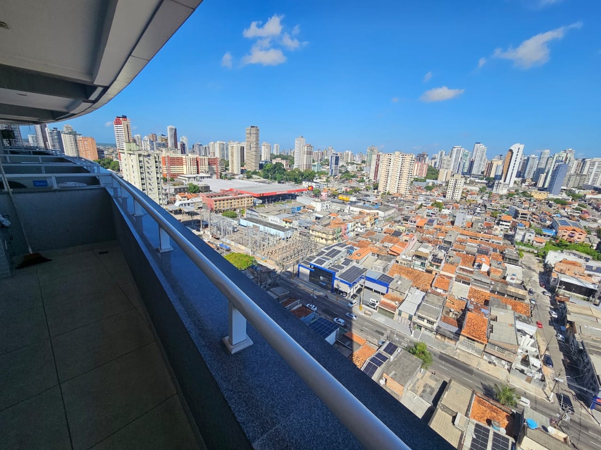 A panoramic view of the urban skyline is showcased from a spacious balcony. The vibrant cityscape reveals a mix of modern high-rises and traditional rooftops under a clear blue sky, offering a glimpse of the dynamic environment below.