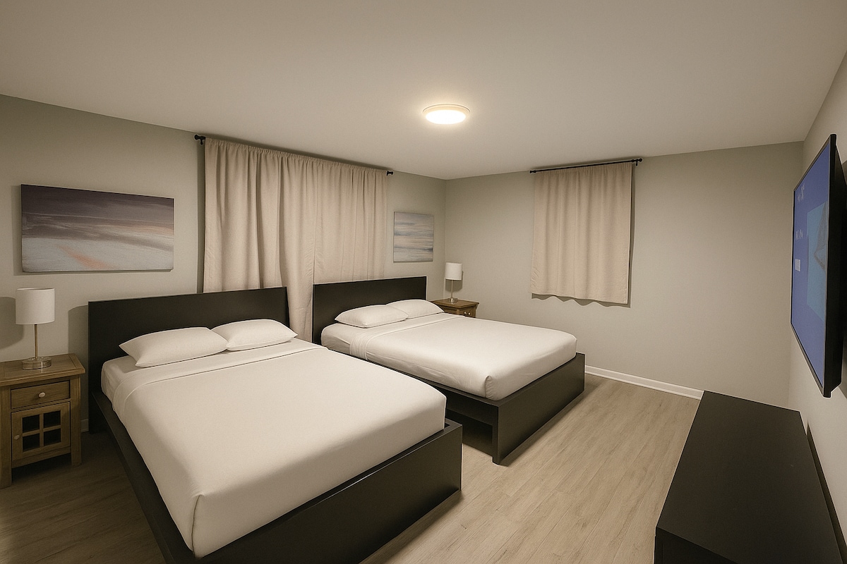 חדר שינה זוגי מודרני ונעים הכולל שתי מיטות קווין סייז עם מצעים שחורים מלוטשים, תאורה רכה ועיצוב אופנתי. כולל טלוויזיה חכמה עם רוקו, שידות לילה אלגנטיות עם מנורות חמות וגוונים נייטרליים לשהייה רגועה.