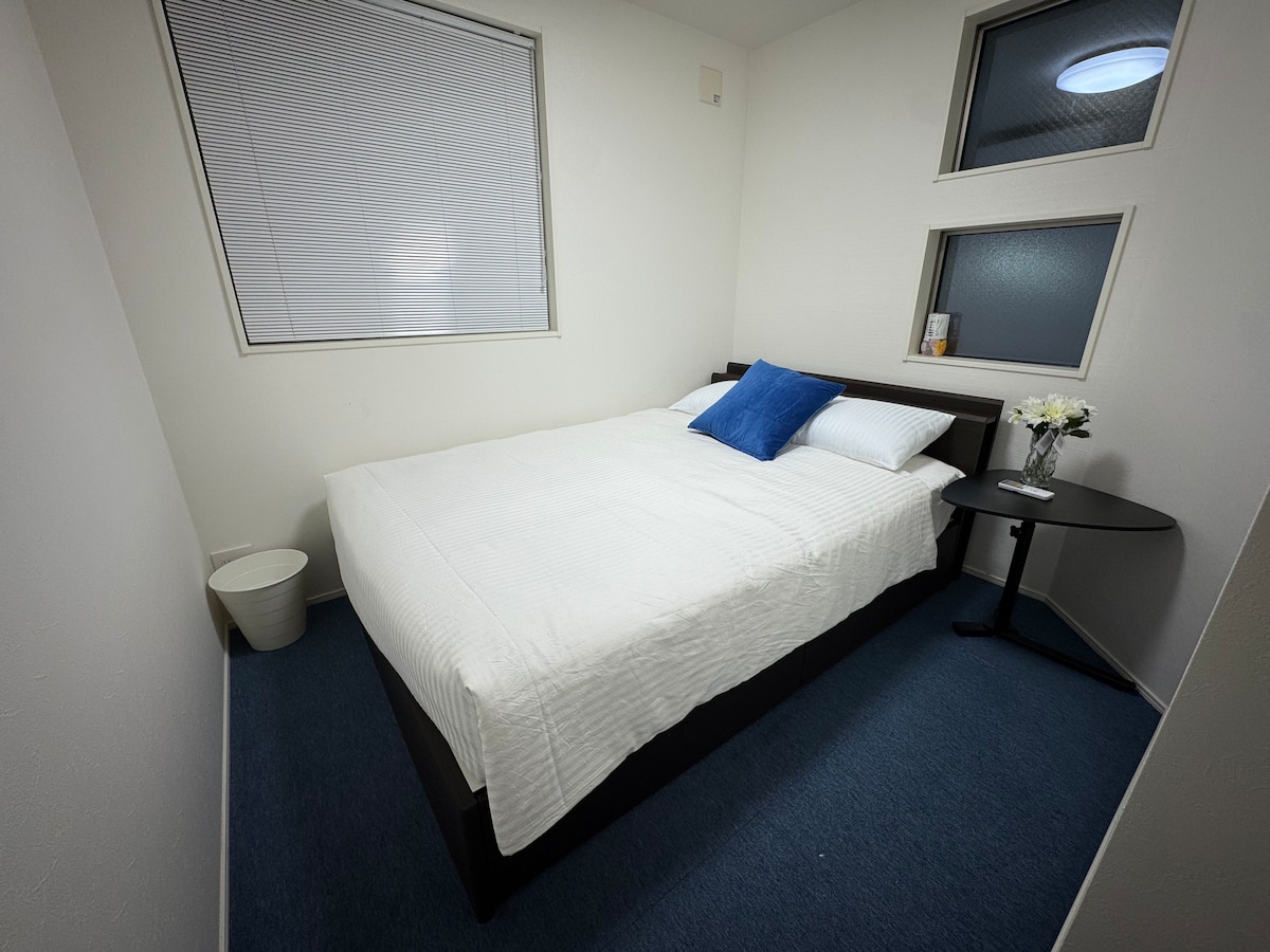 חדר שינה נעים עם מיטה זוגית מרווחת, שולחן קטן ואחסון נוח כולל מדפים לתיקים וארון מובנה.