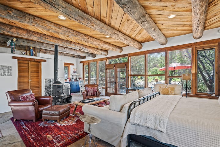 Chumba cha kulala cha kijijini kilicho na viti, madirisha na milango ya bustani na jiko la kuni linalowaka.