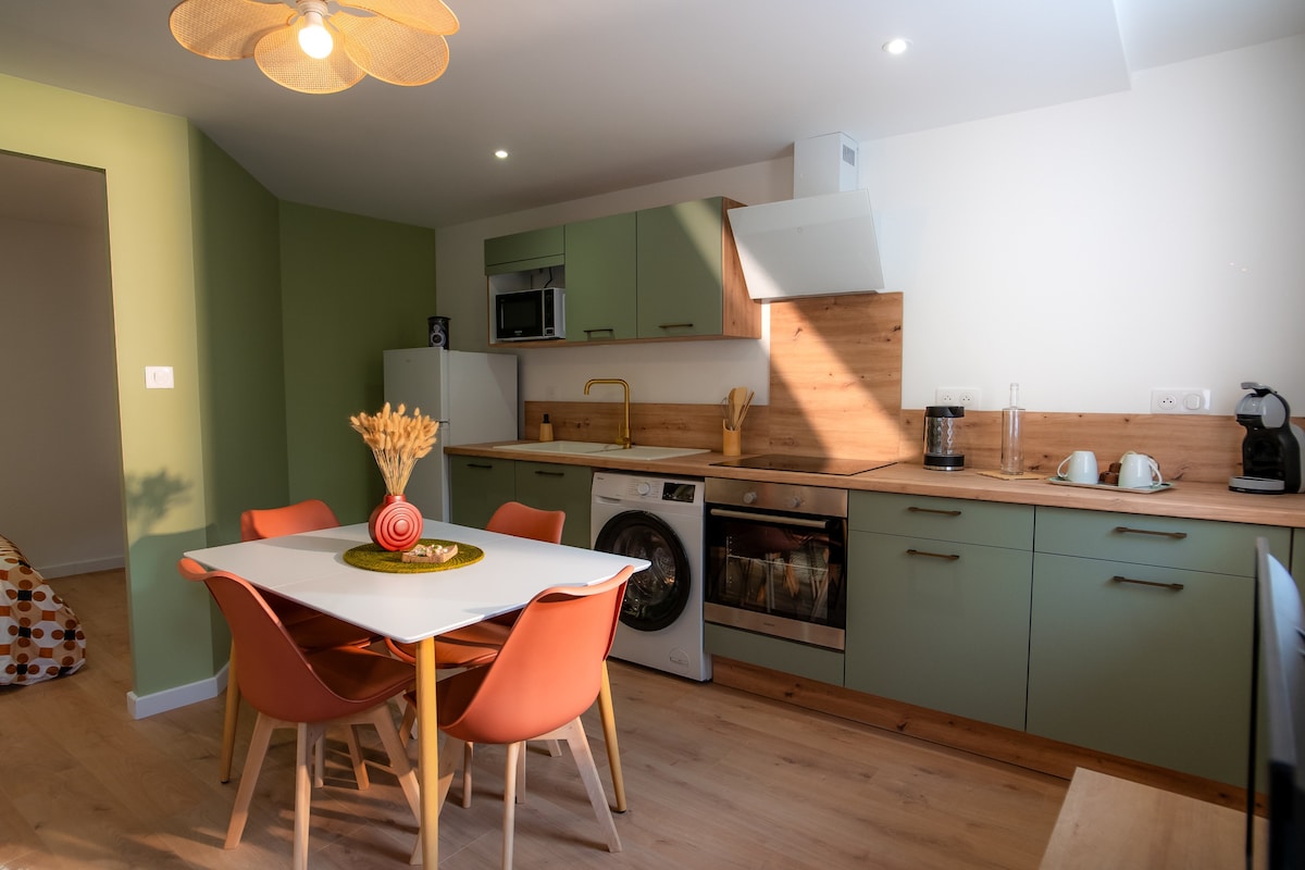 A modern kitchen equipped with essential appliances is featured, including a stove, microwave, and coffee maker. A dining table with four chairs sits at the center, while a stylish light fixture hangs above. Warm wood accents complement the contemporary cabinetry.