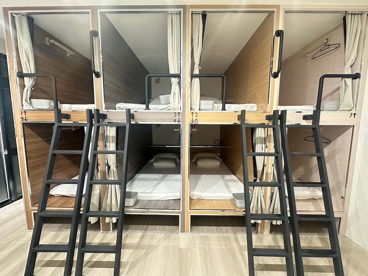 A modern dormitory-style sleeping area features four neatly arranged bunks with wooden frames and ladders. Each sleeping compartment is equipped with bedding and curtains for privacy. Wall hooks provide space for personal belongings, enhancing the overall functionality of the layout.
