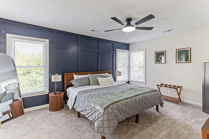 Primary suite featuring a king bed, statement navy accent wall, and corner windows that flood the room with natural light — a relaxing retreat for your stay with Room Darkening Curtains (not shown)