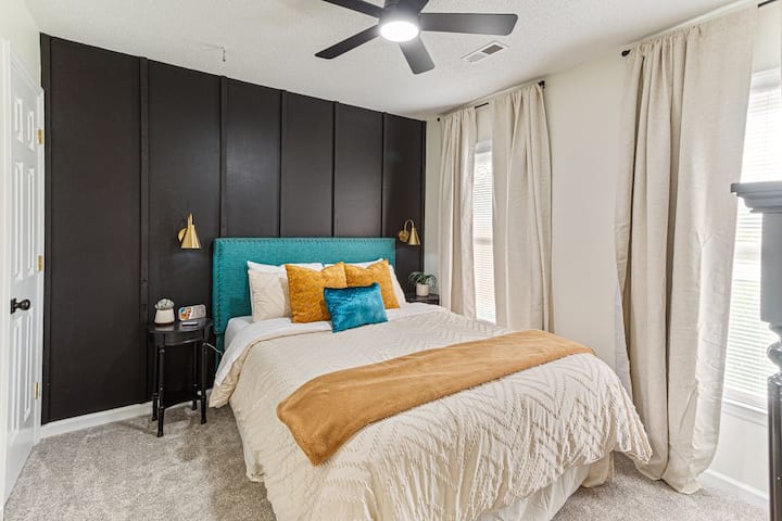 Cozy guest room with a queen bed, bold accent wall, and soft neutral bedding accented with vibrant pillows. Includes a smart TV and dresser for added comfort during your stay.