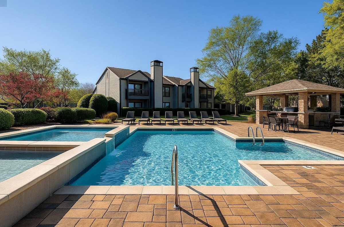 A spacious outdoor pool area features two swimming pools surrounded by laid-back lounge chairs. Lush greenery and well-maintained landscaping add to the serene environment. A covered seating area with tables is situated nearby, offering space for relaxation and gatherings.