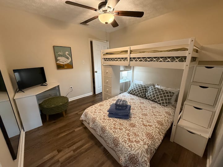 Ორსართულიანი საწოლი, რომელიც სავსეა სამუშაო მაგიდით, კარადით, ტელევიზორითა და სრული ზომის სარკით