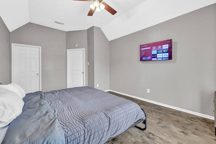 Táto spálňa ponúka útulný priestor so sivými stenami a drevenou podlahou. Je vybavená stropným ventilátorom, nástenným televízorom a dvoma dverami, ktoré ponúkajú moderné a funkčné usporiadanie.