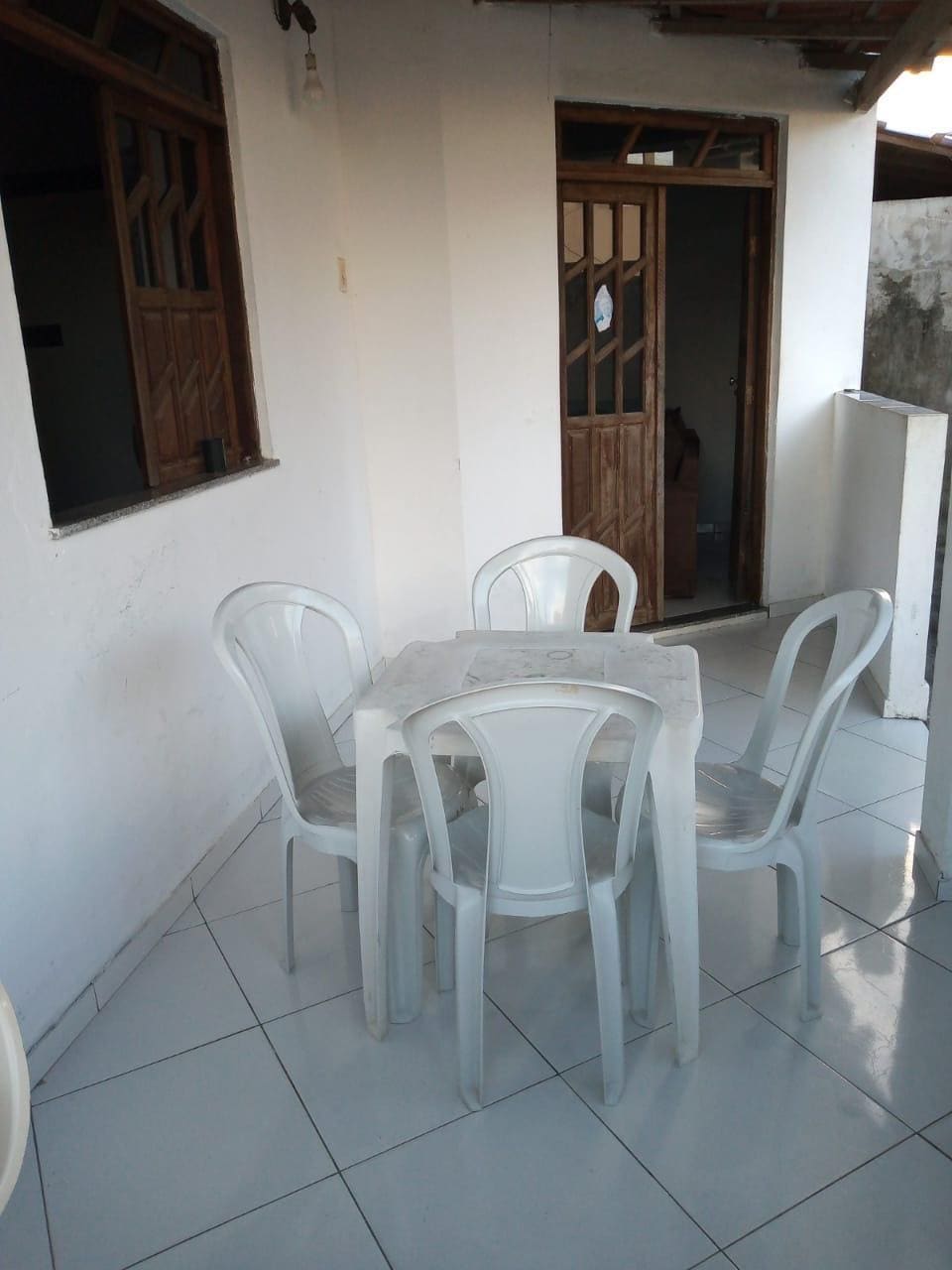 A small outdoor seating area features a round table surrounded by four white chairs. Large windows allow natural light to enter, while the solid wood door leads to another room. The tiled floor adds a clean and polished look to the space.