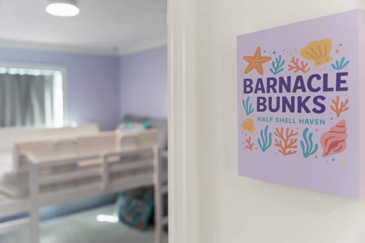 The “Barnacle Bunks” room features bright coastal décor, secure top-bunk safety rails, and a comfy chair for reading or relaxing, an ideal setup for kids, cousins, or extra guests.