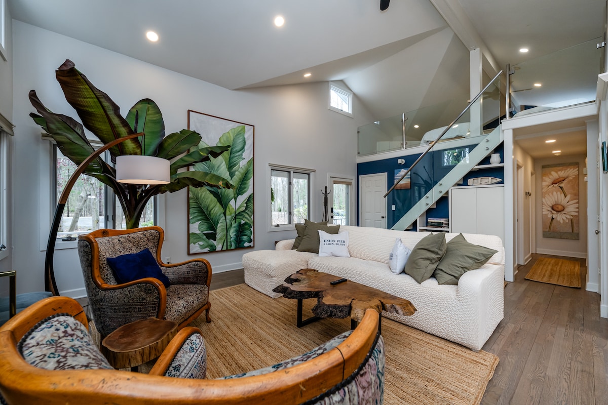 مساحة معيشة مفتوحة ذات سقف مقبب مع سلالم تؤدي إلى منطقة نوم علوية، تكملها طاولة قهوة عضوية، تستحضر جوًا دافئًا وترابيًا وطبيعيًا.