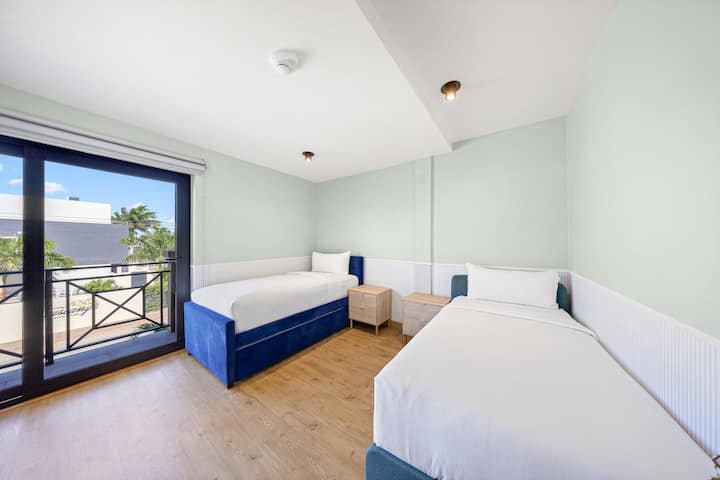 Camera da letto luminosa e ariosa con due letti, testiera blu intenso e balcone con vista panoramica.