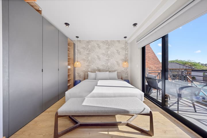 Camera da letto elegante e serena con una parete con motivo a foglie, un ampio armadio a muro e un balcone luminoso con posti a sedere all'aperto.