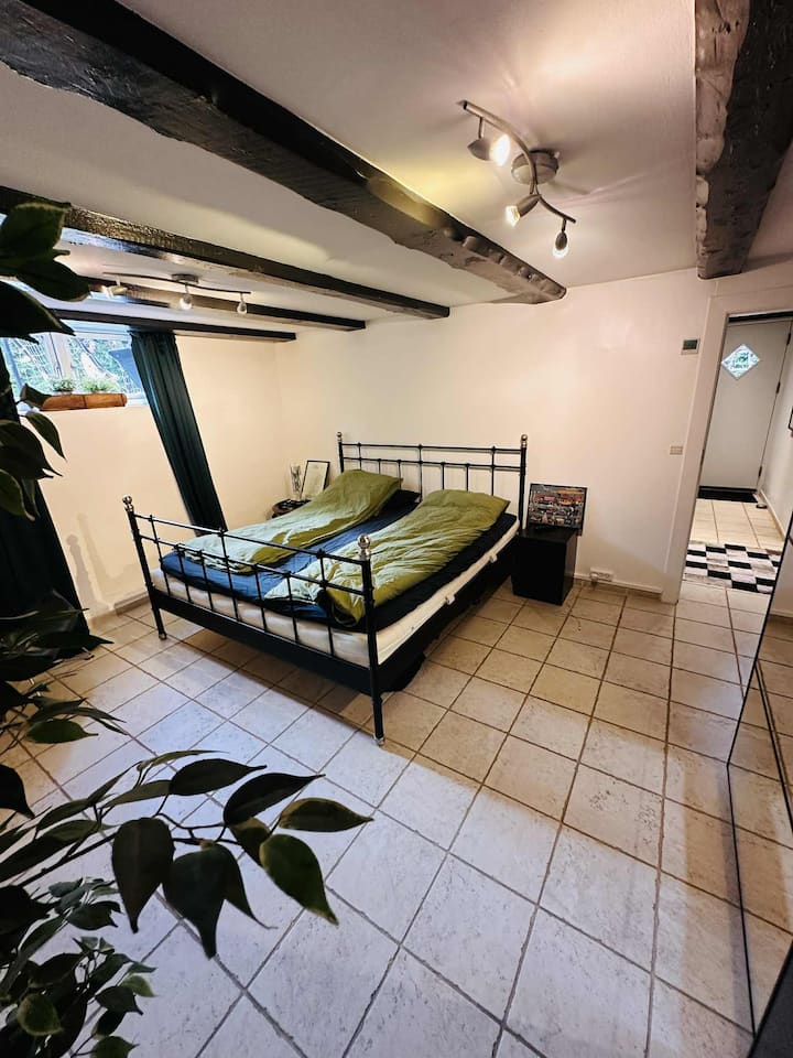 Დიდი საძინებელი ქვედა სართულზე ფანჯრიდან ბაღამდე და უშუქო ფარდებით, ორადგილიანი საწოლი 220x220 სმ, სმარტ-ტელევიზორი YouSee არხების პაკეტით და სტრიმინგის აპებით, სარკე და საწოლისპირა მაგიდები – ფართო მშობლების საძინებელი. Ბავშვის სამოგზაურო საწოლისთვის განკუთვნილი ადგილი.