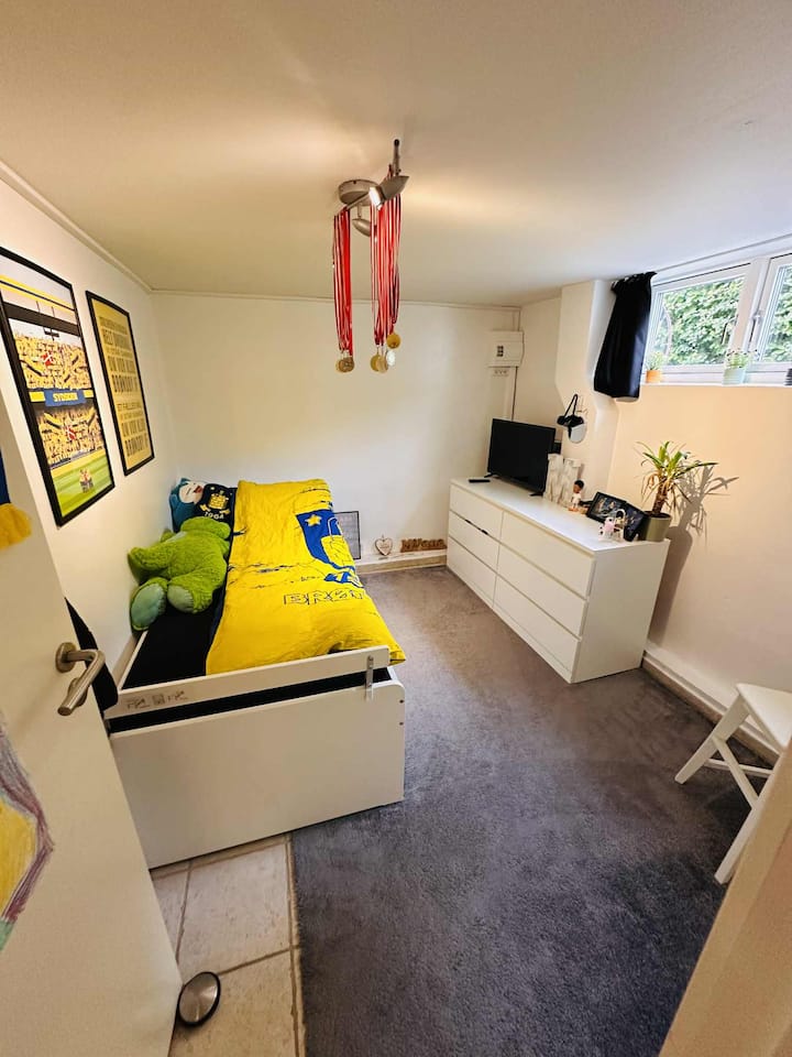 Მყუდრო ოთახი სახლის ქვედა დონეზე, სააბაზანოსთან ახლოს. Საძინებელი სივრცე 1-2 ადამიანისთვის (ზრდასრულებისთვის ან ბავშვებისთვის) 80 × 200 სმ საწოლით და იმავე ზომის გამოსაწევი საწოლით, რომელიც მოთავსებულია საწოლის უჯრაში. Სმარტ-ტელევიზორი სტრიმინგის აპებით – იდეალურია როგორც ბავშვებისთვის, ისე ზრდასრულებისთვის.