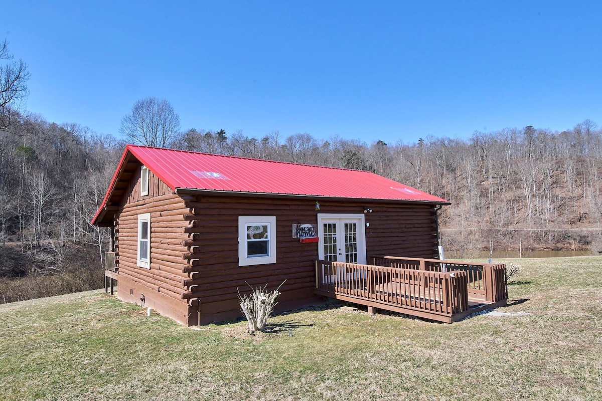 A spacious log cabin is showcased with a vibrant red metal roof. The exterior features large windows and a wooden deck. Surrounded by grassy areas and a view of distant trees, the setting provides a natural and serene atmosphere.