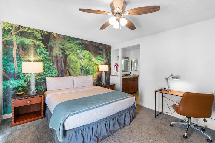 Suite principal con cama king, mural de bosque natural, ventilador de techo, espacio de trabajo dedicado y balcón privado: el refugio definitivo.