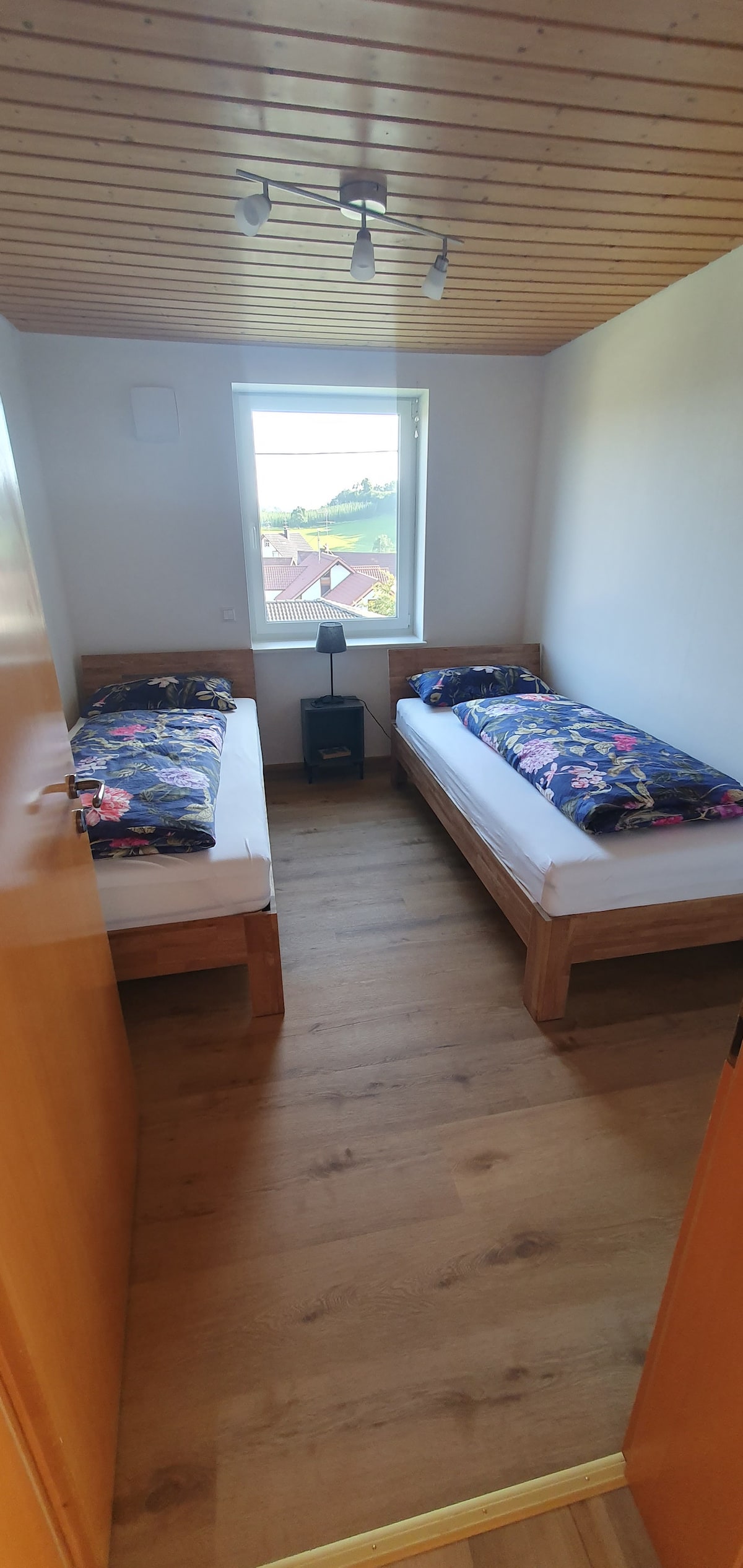 Chumba kidogo cha kulala kina vitanda viwili na meza kando ya kitanda iliyo na taa