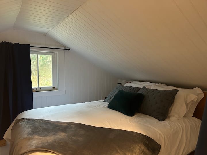 Mirna spavaća soba s pogledom na šumu.  Strop je nagnut s obje strane, pa će gosti morati paziti dok se kreću.