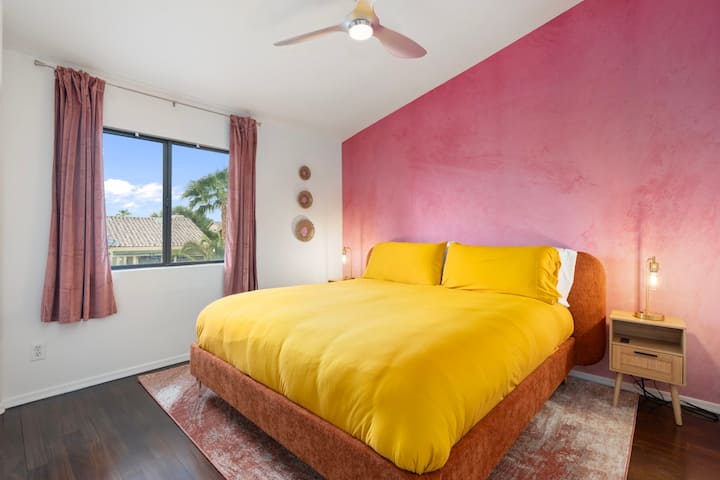 Vibrant and full of warmth — this sunny bedroom features a plush king bed, bold pink accent wall, and modern décor. A cheerful retreat designed for comfort, style, and a restful night’s sleep.
