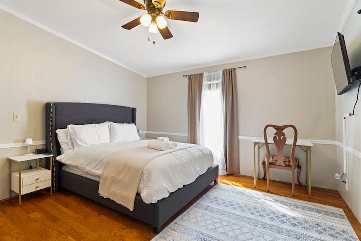 חדר שינה נוח בגודל קווין סייז עם מיטה מרופדת קטיפה, פינת עבודה ייעודית וחלון גדול שממלא את החדר באור טבעי - מושלם למנוחה או לעבודה קצרה במהלך השהייה