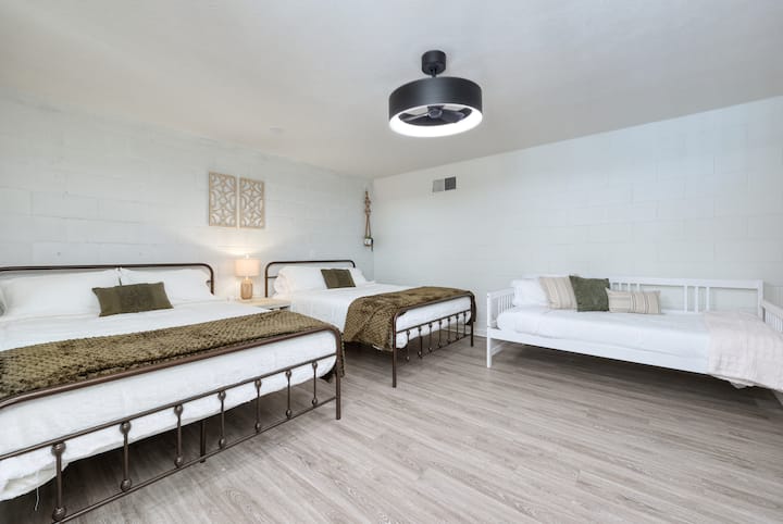 Spálňa v suteréne s bielou stredovou stenou. 2 manželské postele + 1 dvojlôžková pohovka.