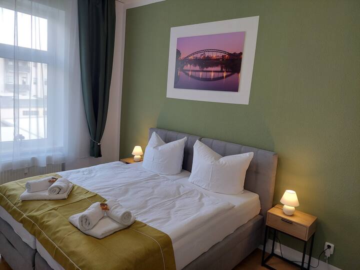 Dormitorio con dos camas, tres toallas, pared verde y mural.