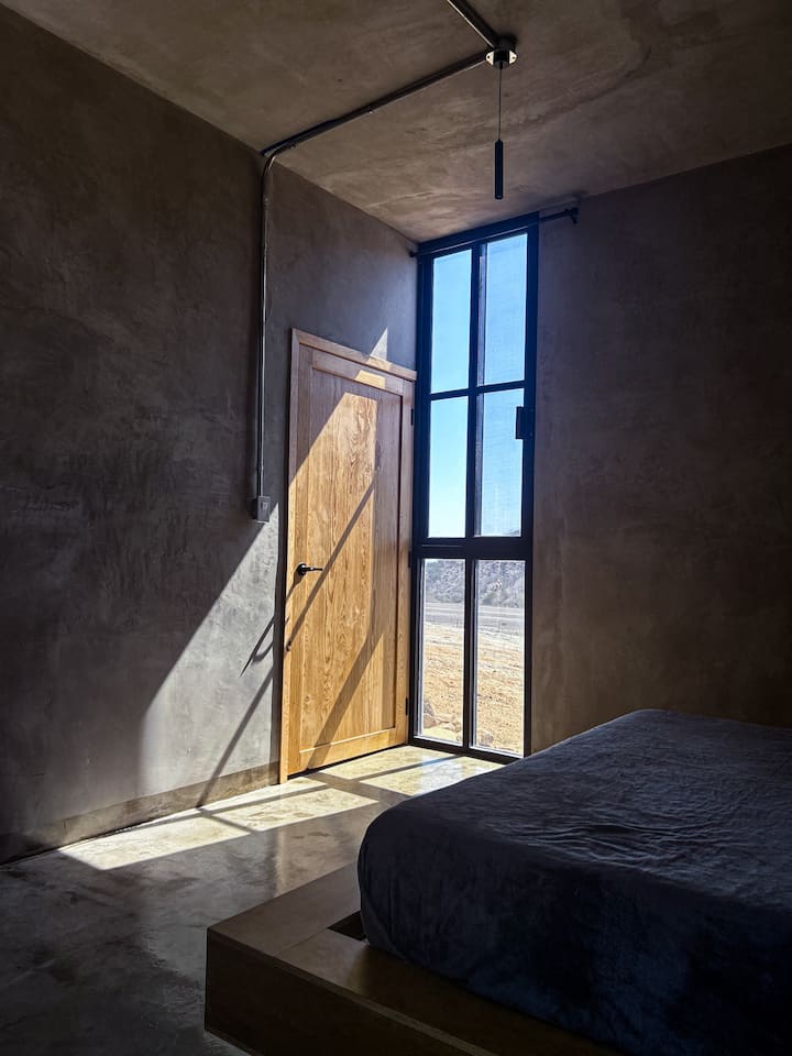 سرير بحجم كوين، وأريكة، وباب دخول إلى الحمام. نوافذ عالية تطل على التلال الصحراوية. 