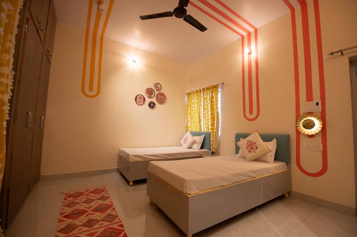Cette chambre à coucher allie l'élégance du Rajasthan à une touche moderne. Elle est dotée de deux lits simples, de murs décorés d'art moderne, de rideaux jaunes joyeux et d'une armoire spacieuse. Profitez du confort de la climatisation et d'une salle de bain privée attenante pour un séjour détendu et élégant.